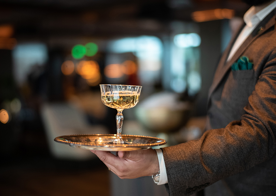 A waiter carrying a golden plate with a glass of wine on top