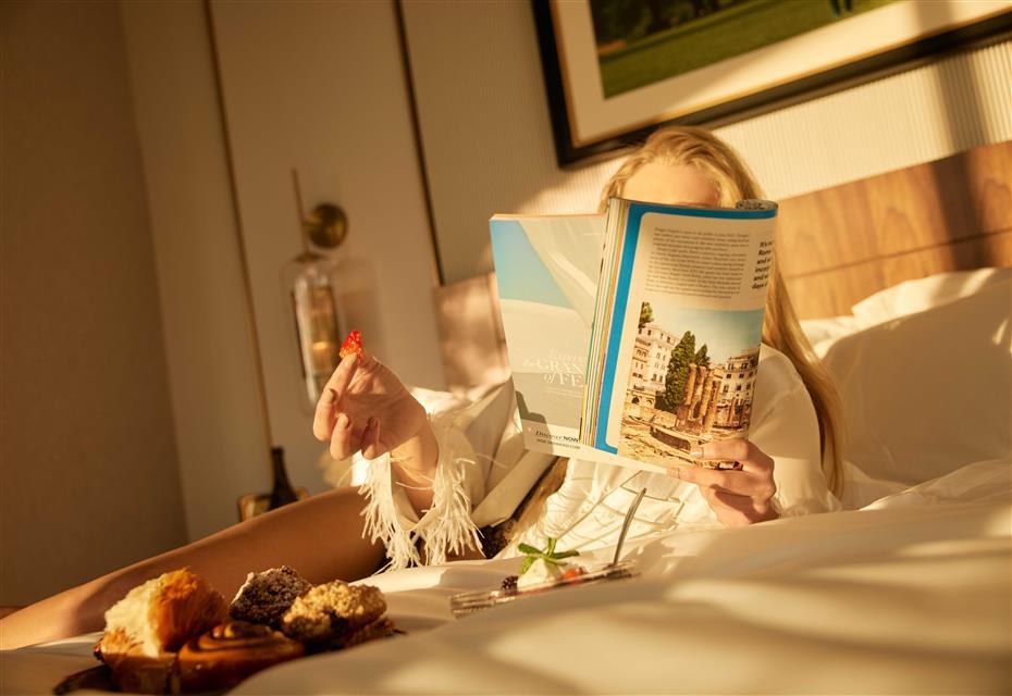 Girl in bed eating room service and reading a magazine